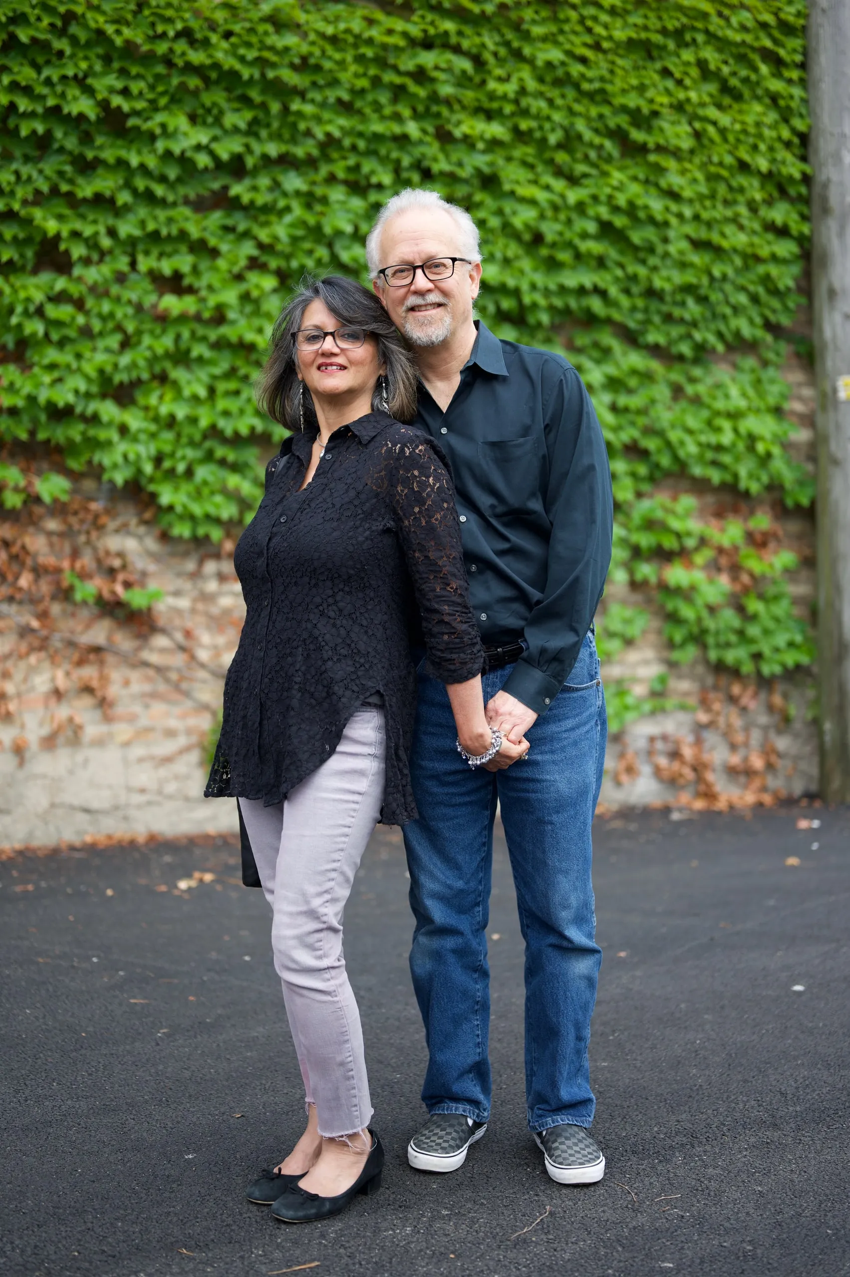 A couple standing hand in hand in front of an ivy-covered wall