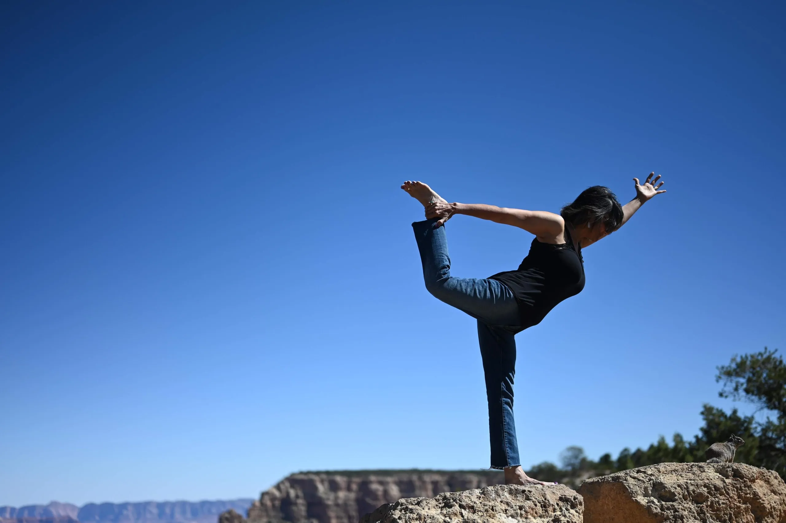 A woman holding a dancer's yoga pose on a rocky ledge under a deep blue sky