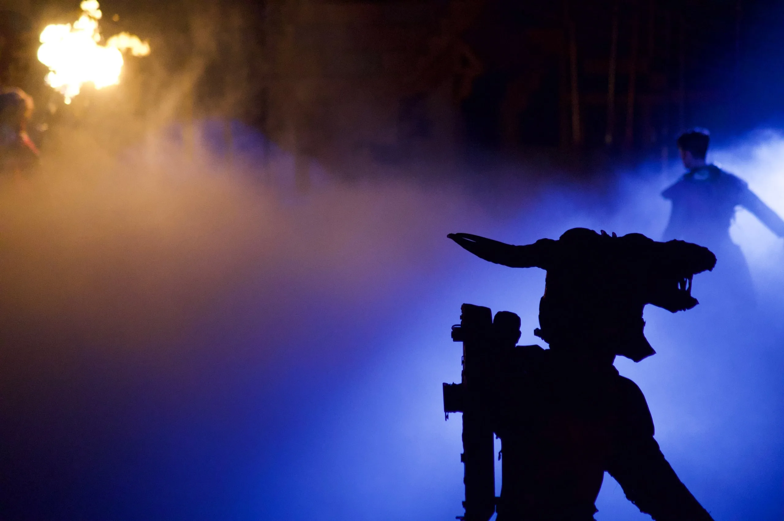 A fire performer silhouetted against blue light and smoke